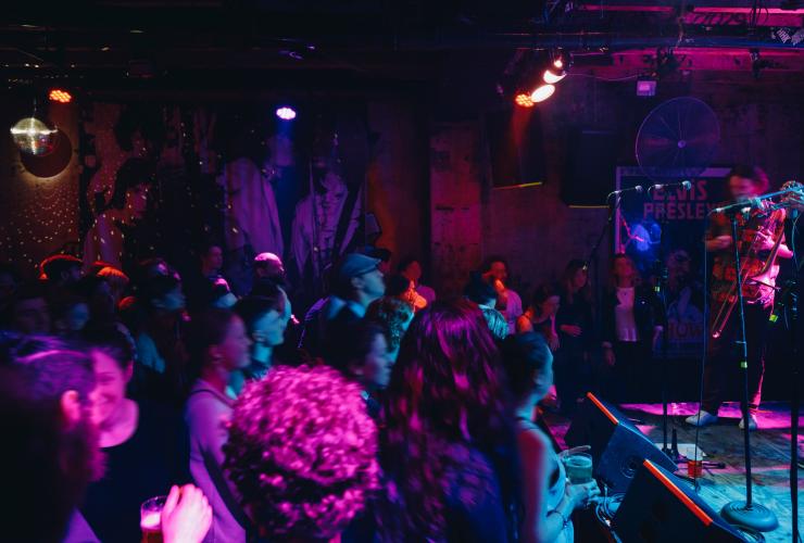 A crowd of people watching a band perform on stage beneath colourful lights in a dimly lit venue at Cherry Bar, Melbourne, Victoria © Visit Victoria