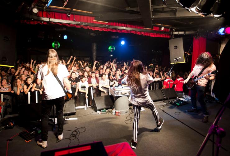 View from behind a band performing on stage with a crowd of people waving their hands in the air in front of them at the Corner Hotel, Richmond, Victoria © Zo Damage