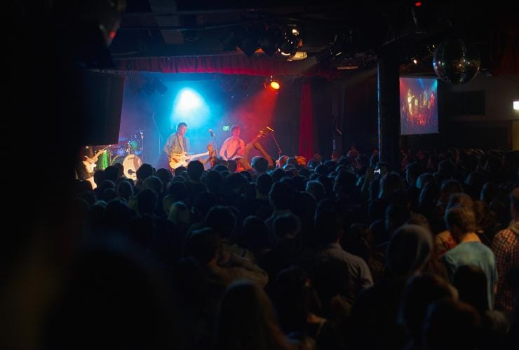 A crowd of people dancing in front of a live band performing on a stage under blue and red lights at the Corner Hotel, Richmond, Victoria © Visit Victoria
