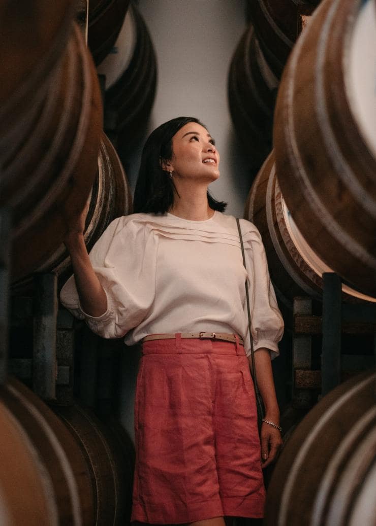 Woman standing among wooden barrels at Hoochery Distillery Cafe in Kununurra, Western Australia © Tourism Western Australia