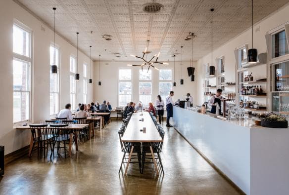 Thực khách đang dùng bữa trong không gian ngập tràn ánh sáng với chiếc bàn dài ở giữa tại Agrarian Kitchen Eatery, Thị trấn New Norfolk, Tiểu bang Tasmania © Adam Gibson 