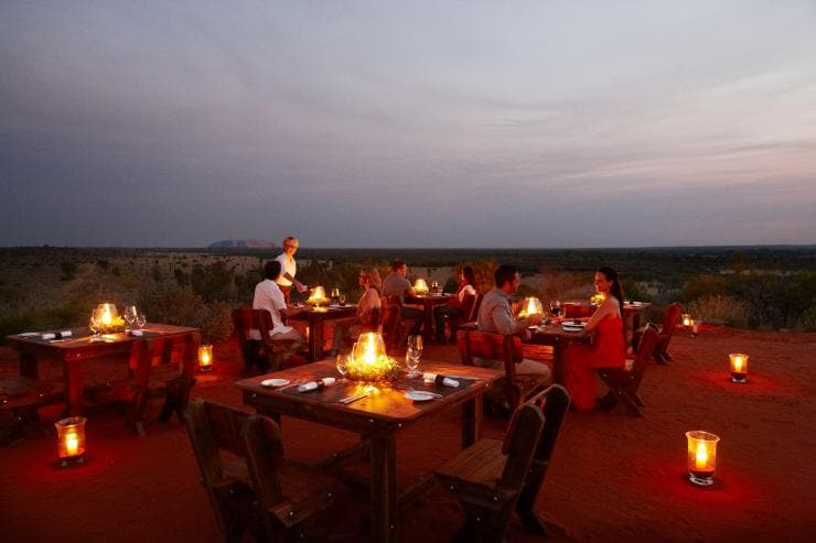 A group of people dining outdoors at dusk with Uluru behind them at Tali Wiru, Uluru, Northern Territory © Tali Wiru