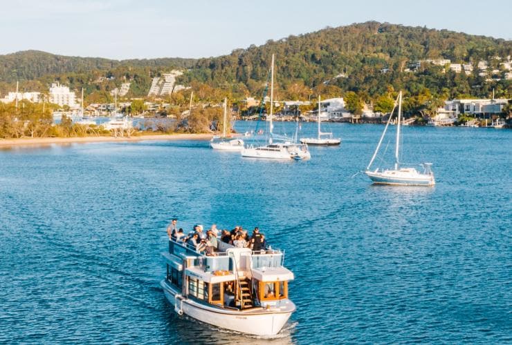 Aerial view over a boat decked with people with a lush green coastline in the distance during Noosa Eat & Drink Festival, Noosa, Queensland © Tourism and Events Queensland 