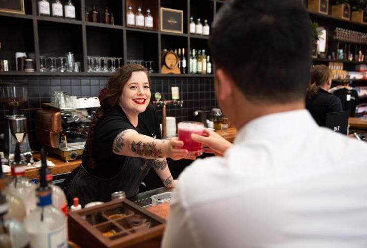 A bartender handing a customer a bright pink cocktail at Four Pillars Gin, Healesville, Victoria © Visit Victoria 