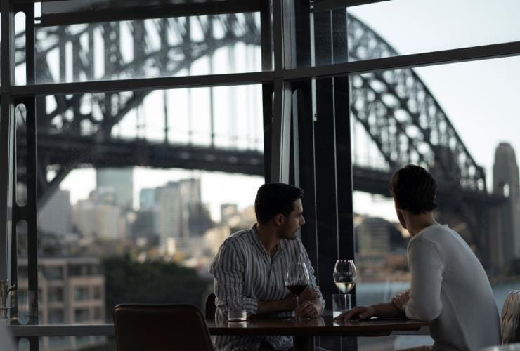 A couple with a view of the Sydney Harbour Bridge behind them at Quay Restaurant, Sydney, New South Wales © Destination NSW