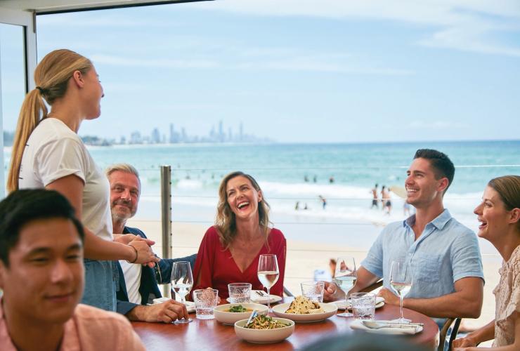 Diners smiling at an ocean-front table at Rick Shores, Burleigh Heads, Queensland © Tourism and Events Queensland