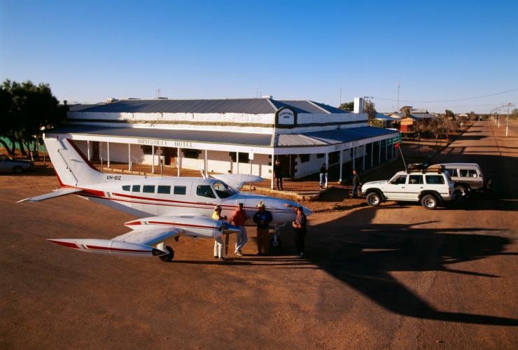 Aerial view over a small plane parked outside a historic pub with a group of people gathered around drinking and chatting at Birdsville Hotel, Queensland © Tourism Australia