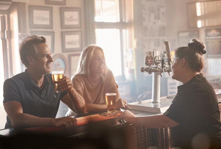 Couple enjoying a beer at a bar while speaking to a bartender at Silverton Hotel, Silverton, New South Wales © Destination NSW