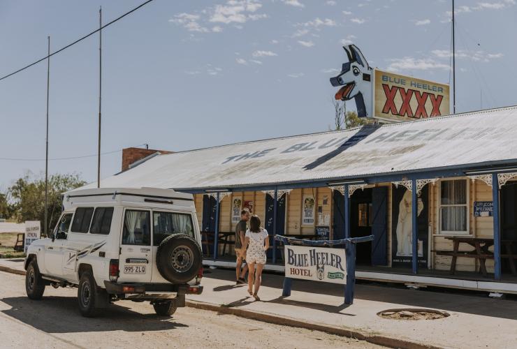 Two people walking into a venue with a blue cartoon dog on its roof at the Blue Heeler Hotel, Kynuna, Queensland © Tourism and Events Queensland 