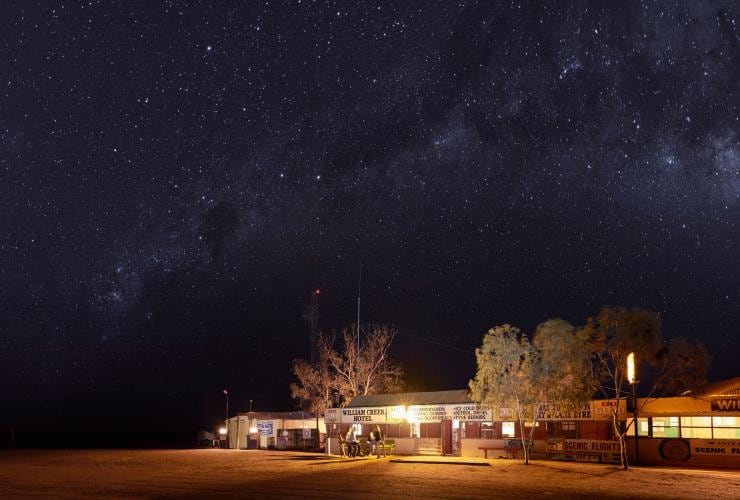 The exterior of a building glowing from lights inside beneath a star-filled sky at night at William Creek Hotel, Flinders Ranges & Outback, South Australia © South Australian Tourism Commission