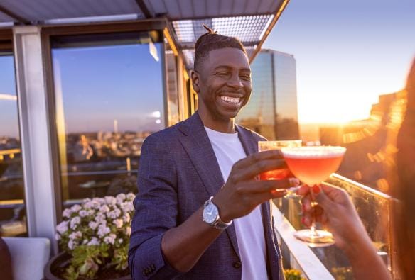 A couple clinks their drinks as the sun sets on the rooftop of Aster, Sydney, New South Wales © Tourism Australia 