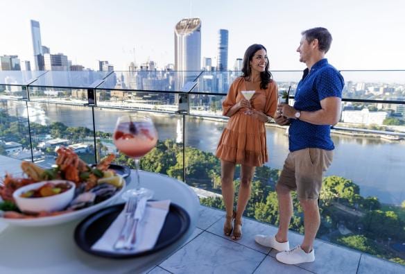 A couple drinking cocktails with the Brisbane skyline in the background at The Terrace Rooftop Bar, Brisbane, Queensland © Tourism Australia 