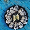 Aerial view over a plate of oysters spread out in a circle with lemon wedges in the centre on a blue table with Get Shucked, Bruny Island, Tasmania © Adam Gibson/Tourism Tasmania
