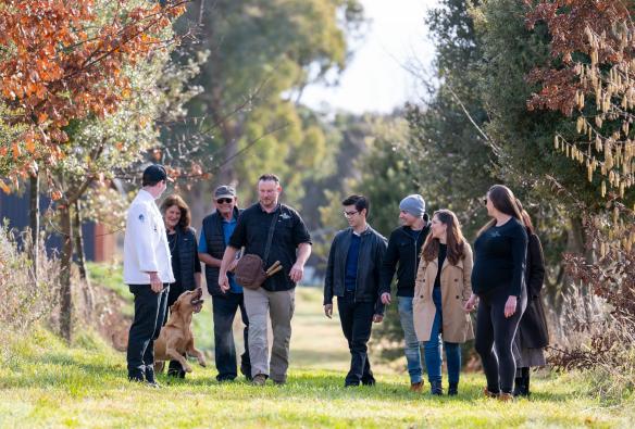 A group of people searching for truffles with a dog between two rows of trees at The Truffle Farm, Majura, Australian Capital Territory © Tourism Australia