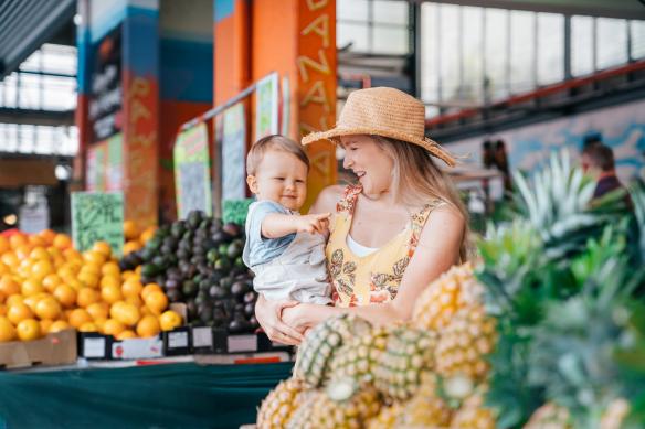 Một người mẹ và đứa trẻ đang tham quan chợ nông sản đầy màu sắc với các sạp trái cây tươi ngon, Rusty’s Markets, Thành phố Cairns, Tiểu bang Queensland © Tourism and Events Queensland