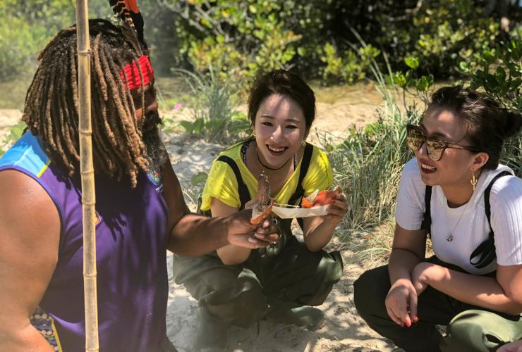 Three people crouched down on a grassy beach holding crab legs with Tweed Eco Cruises, Tweed Heads, New South Wales © Tweed Eco Cruises
