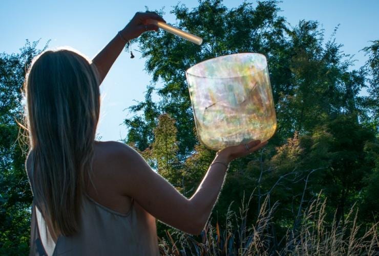 A person standing outside among bushland on a clear day holding a sound bath and wand at Samadhi Retreat, Daylesford, Victoria © Samadhi Retreat