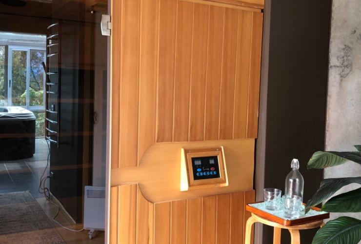 The exterior of a sauna with a wooden door, a hot tub in the background and water glasses in the foreground at Harmony Hill Health Retreat, Hobart, Tasmania © Harmony Hill Health Retreat