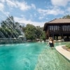 A woman walking along a ledge inside a clear blue pool with a water fountain nearby and a wooden building behind her on Makepeace Island, Noosa, Queensland © Makepeace Island