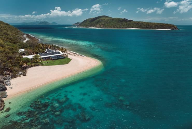 Aerial view over an island with a white sand shore and clear blue water and another island in the distance at Pelorus Private Island, Palm Island, Queensland © Jason Lerace/Pelorus Private Island