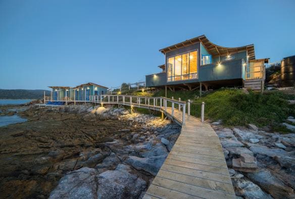 Close up on a pier over the calm ocean looking toward two buildings with large windows at night on Picnic Island,  Coles Bay, Freycinet, Tasmania © Picnic Island Pty Ltd