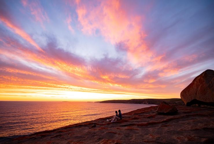 Two people sitting in front of the Remarkable Rocks overlooking the ocean during a bright pink and orange sunrise, Kangaroo Island, South Australia © Tourism Australia