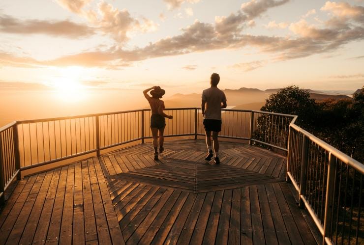 Two people walking towards the railing of Boroka Lookout with the sun lighting up the sky during sunrise, Grampians National Park, Victoria © Visit Victoria