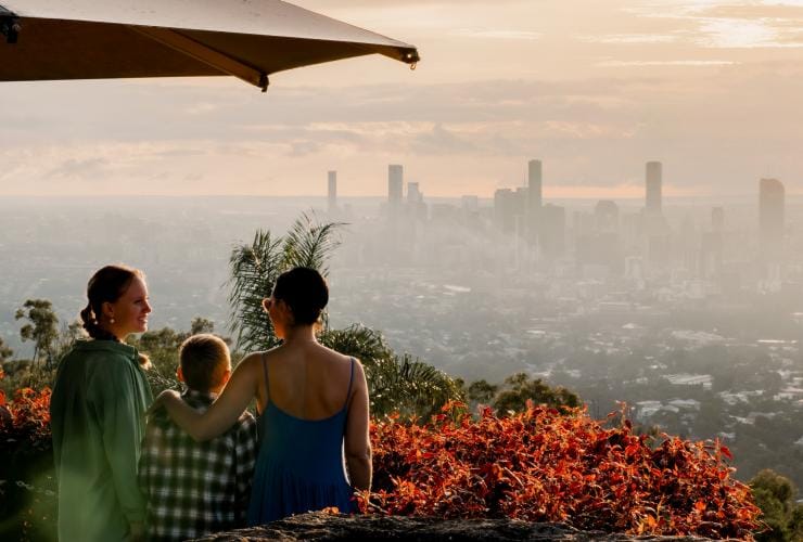 A family standing among flowers and plants overlooking the Brisbane skyline during sunrise at Mount Coot-Tha Lookout, Brisbane, Queensland © Tourism and Events Queensland