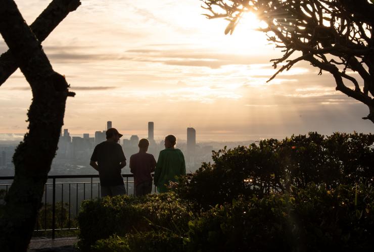 Trees in the foreground with a family standing behind them, overlooking the Brisbane skyline from Mount Coot-Tha Lookout, Brisbane, Queensland © Tourism and Events Queensland
