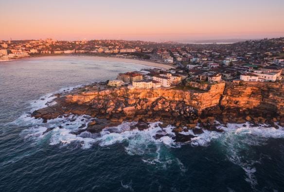 Aerial view over the coastline surrounding Bondi Beach glowing pink and orange during sunrise, Sydney, New South Wales © Tourism Australia