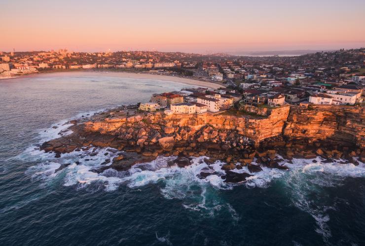 Aerial view over the coastline surrounding Bondi Beach glowing pink and orange during sunrise, Sydney, New South Wales © Tourism Australia