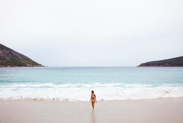 Woman emerging from the ocean onto white sand at Wineglass Bay Beach, Freycinet National Park, Tasmania © Sean Scott