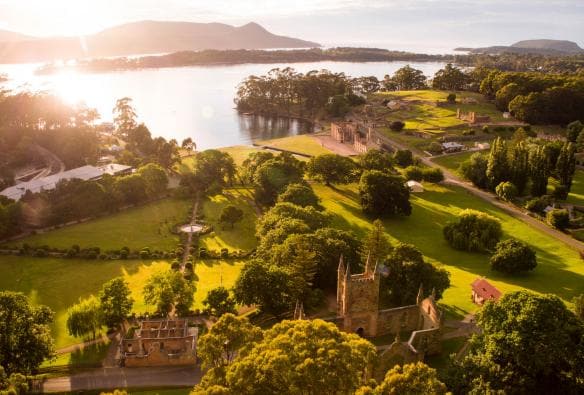 Ảnh chụp từ trên cao ánh nắng chiếu xuống Di tích lịch sử Port Arthur, được bao quanh bởi cây cối và làn nước trong xanh tĩnh lặng ở Port Arthur, Tiểu bang Tasmania © Alastair Bett
