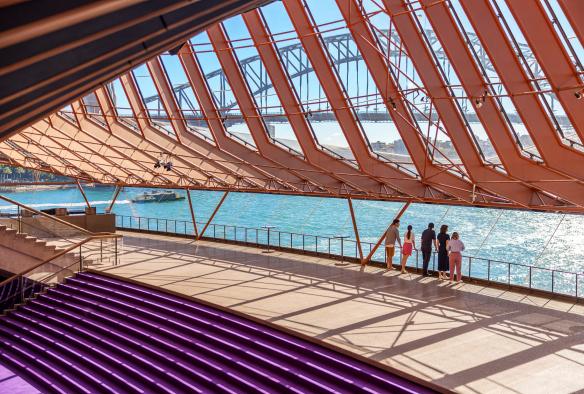 Một nhóm du khách đang đắm mình trong chuyến tham quan kiến trúc Nhà hát Opera Sydney, đứng từ rìa nhà hát nhìn ra Cảng Sydney, Thành phố Sydney, Tiểu bang New South Wales © Tourism Australia