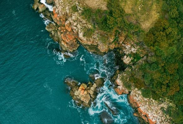 Aerial view of the Bruny Island coastline, with orange lichen-covered rocks, blue water and lush greenery in Tasmania © Georges Antoni