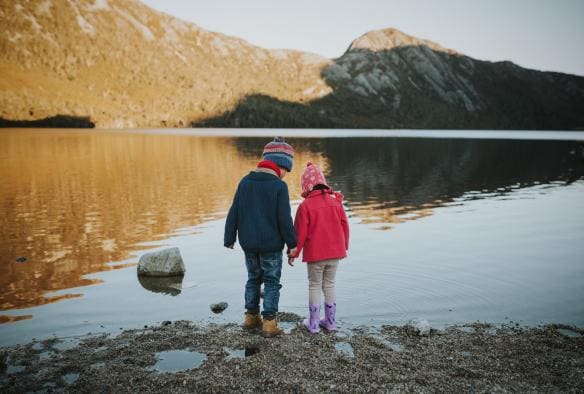 Two children looking at their reflection on the glassy surface of Dove Lake in Cradle Mountain-Lake St Clair National Park, Tasmania © Laura Helle