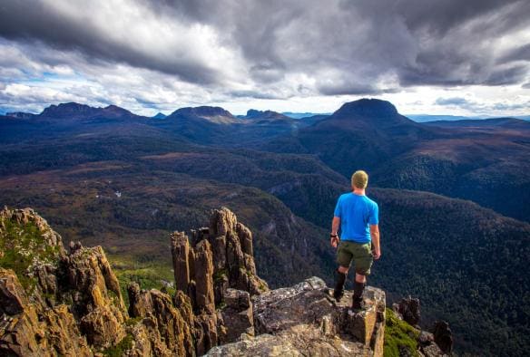Man standing on a rock overlooking the wilderness on the Cradle Mountain Huts Overland Track Walk in Cradle Mountain-Lake St Clair National Park, Tasmania © Tasmanian Walking Company/Great Walks of Australia