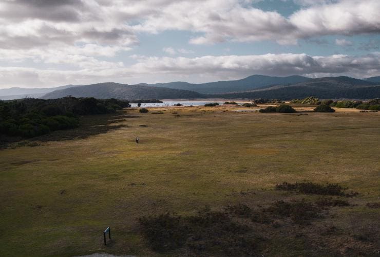 Aerial view of grassy plain, mountains, trees and a waterway at Springlawn, Narawntapu National Park, Tasmania © Samuel Shelley