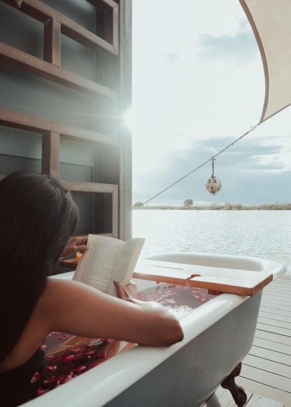 Một người đang đọc sách trong bồn tắm đầy cánh hoa hồng trên ban công ven sông, Bill's Boathouse, Sông Murray, Tiểu bang Nam Úc © Bash_Images/South Australian Tourism Commission