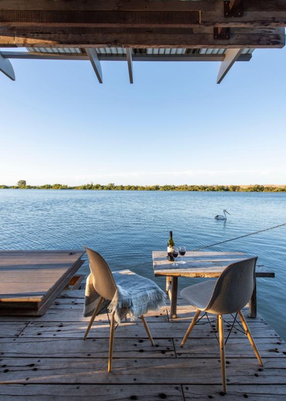 Một chiếc bàn bày rượu vang đỏ trên ban công nhìn ra sông khi chú chim bồ nông bơi ngang qua, Bill's Boathouse, Sông Murray, Tiểu bang Nam Úc © Bash_Images/South Australian Tourism Commission