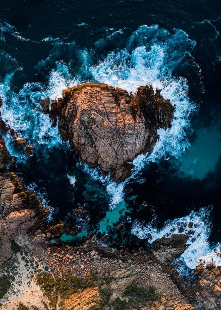 Ảnh chụp từ trên cao chụp khối đá Sugarloaf Rock, xung quanh là những con sóng trắng và xanh đang đập vào khối đá đó ở vùng Margaret River, Tây Úc © Tourism Australia