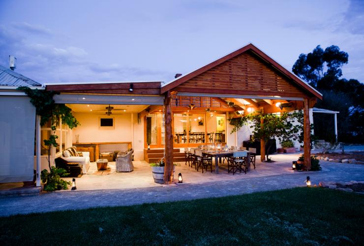Exterior of a homestead in the evening, with lanterns strewn along the pavement, a cosy outdoor lounge area and a large dining table set on a patio at Arkaba Station, Flinders Ranges, South Australia © Wild Bush Luxury