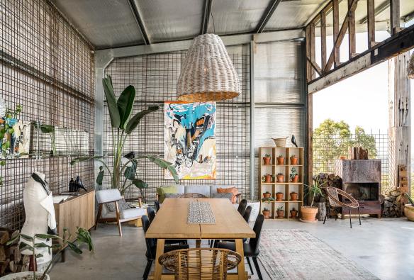 A large, open room with a dining table, artworks and pot plants and an open wall letting in sunlight at Blackbird, Bryon Bay, New South Wales © Blackbird/Saul Goodwin @propertyshotphotography