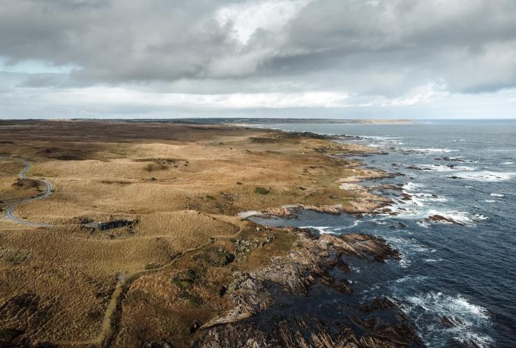 An aerial view over a sleek, black building on a grassy hill overlooking a rugged coastline at Kittawa Lodge, King Island, Tasmania © Kittawa Lodge/Oscar Sloane