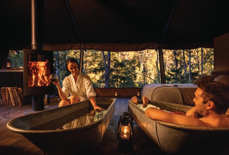 A couple enjoying twin indoor baths beside a fireplace at Nightfall Camp, Lamington National Park, Queensland © Nightfall Camp