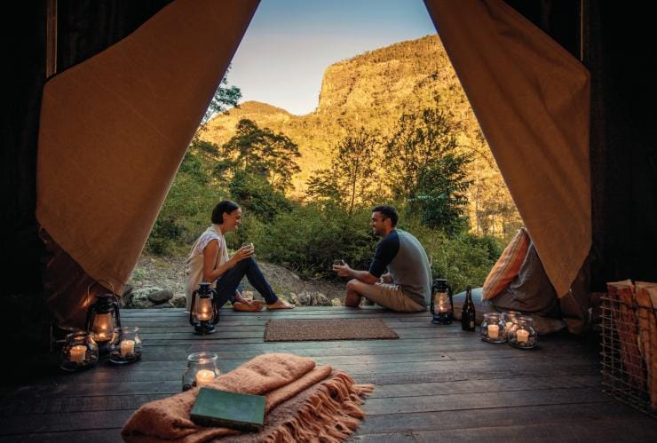 View from inside a glamping tent looking out at two people sitting on the wooden floor surrounded by candles overlooking bushland at Nightfall Camp, Lamington National Park, Queensland © Nightfall