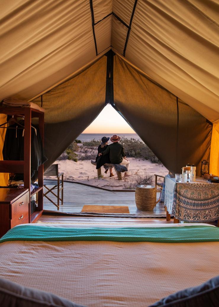 View looking out through the opening of a tent towards two people sitting on a balcony overlooking the ocean at Sal Salis, Ningaloo Reef, Western Australia © Sal Salis Ningaloo Reef
