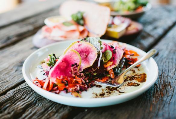 A colorful fresh salad topped with vibrant pink radish slices sits on a rustic wooden table at Three Blue Ducks in Byron Bay, New South Wales © Destination NSW