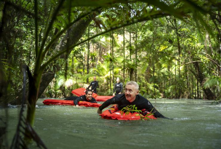 A group of people floating on inflatable red rafts on top of a river surrounded by lush green rainforest with Back Country Bliss Adventures, Daintree, Queensland © Tourism Tropical North Queensland