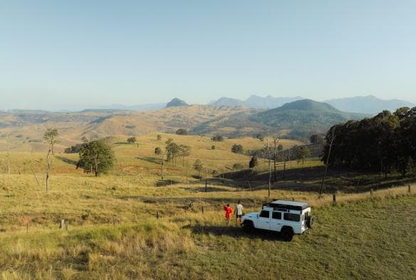 Hai người đang đứng cạnh một chiếc xe địa hình 4WD giữa vùng nông thôn xanh tươi, Baya Tiny House, Scenic Rim, Tiểu bang Queensland © Tourism and Events Queensland